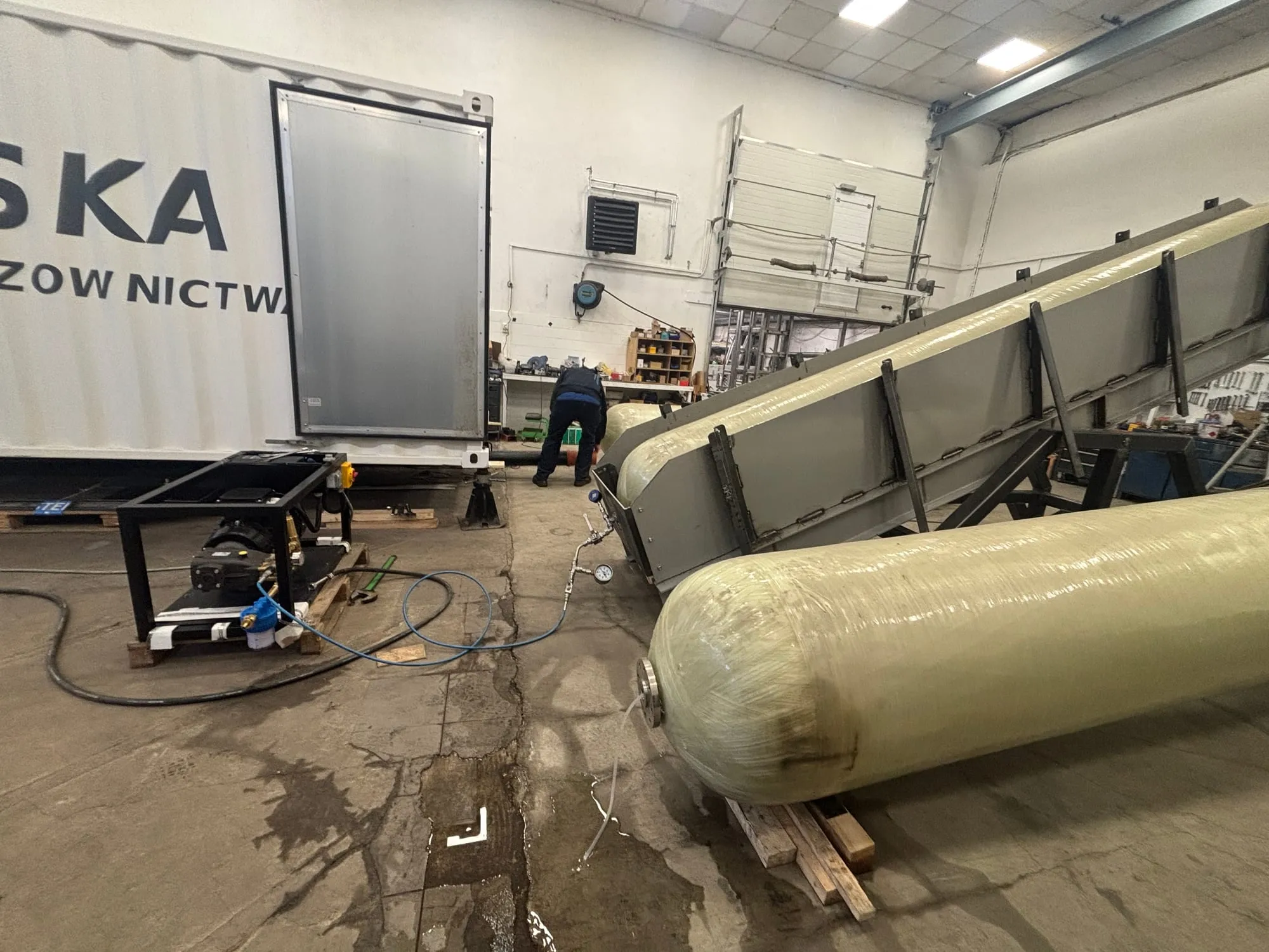 Hydraulic pressure test in progress on a cylinder in the Gaznet workshop, pump and gauge connected, customer container behind